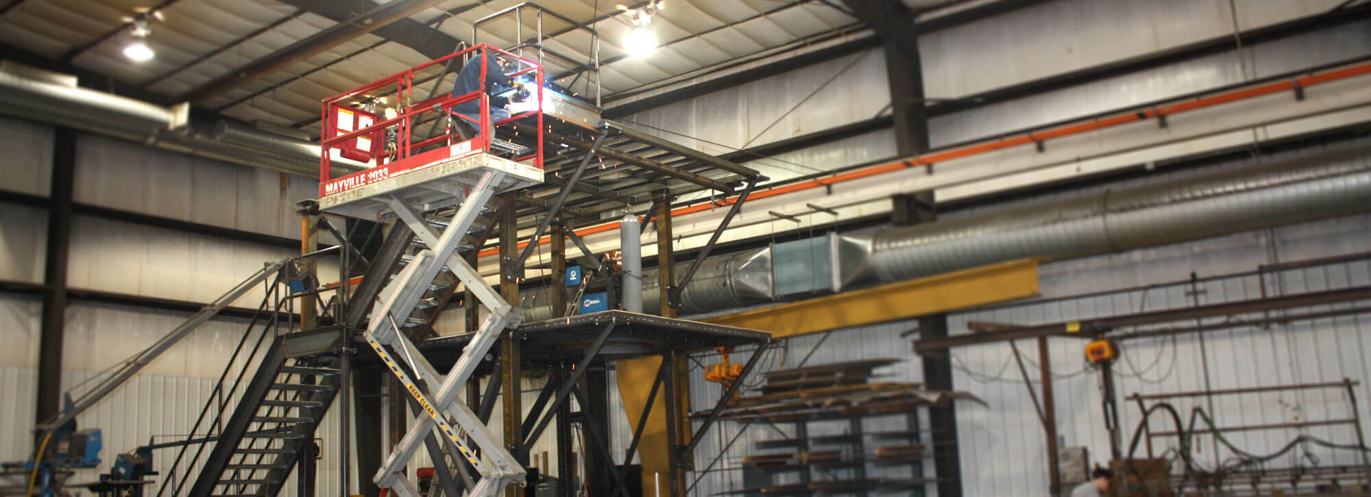 Fabricators at Millwood Metalworks using a scissor lift to weld on a large stair structure