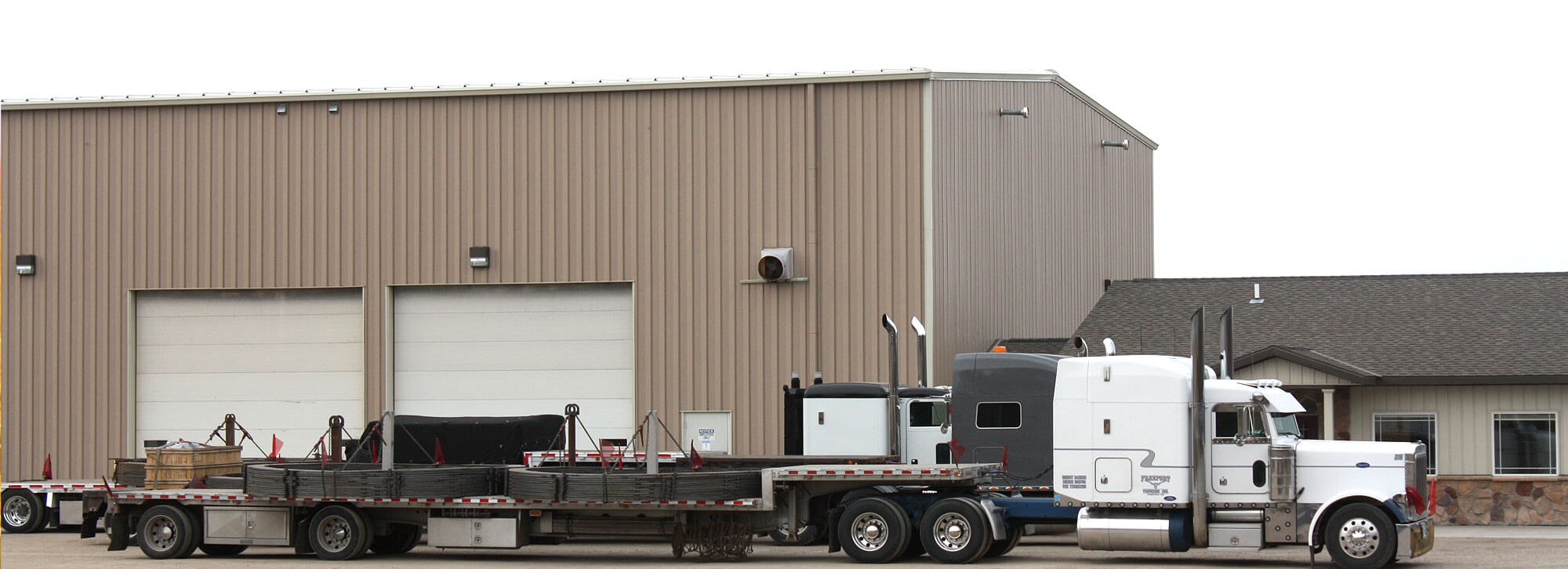 Semi tractors with flatbed trailers loaded with wind turbine embed rings sitting in front of Millwood Metalworks' fabrication shop in Freeport, MN